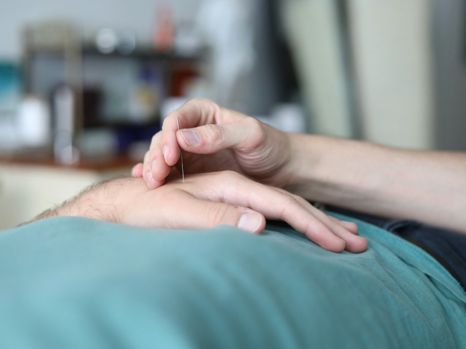 An acupuncturist's hand resting gently beside a needle in a patient's hand